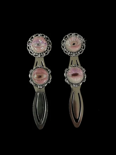 Two distinct handcrafted seashell eyeball bookmarks with different lash and iris styles, photographed from a straight-on vertical view.