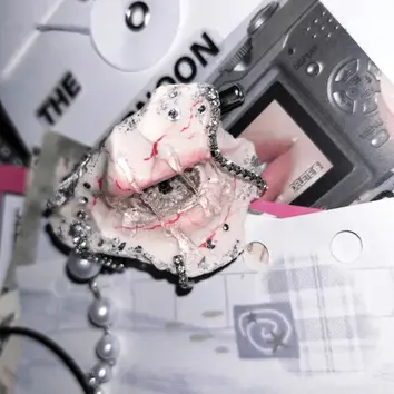 Edgy cyberpunk style eye sculpture inside a shell with red veins, rhinestone trim, and silver chains, next to a vintage digital camera